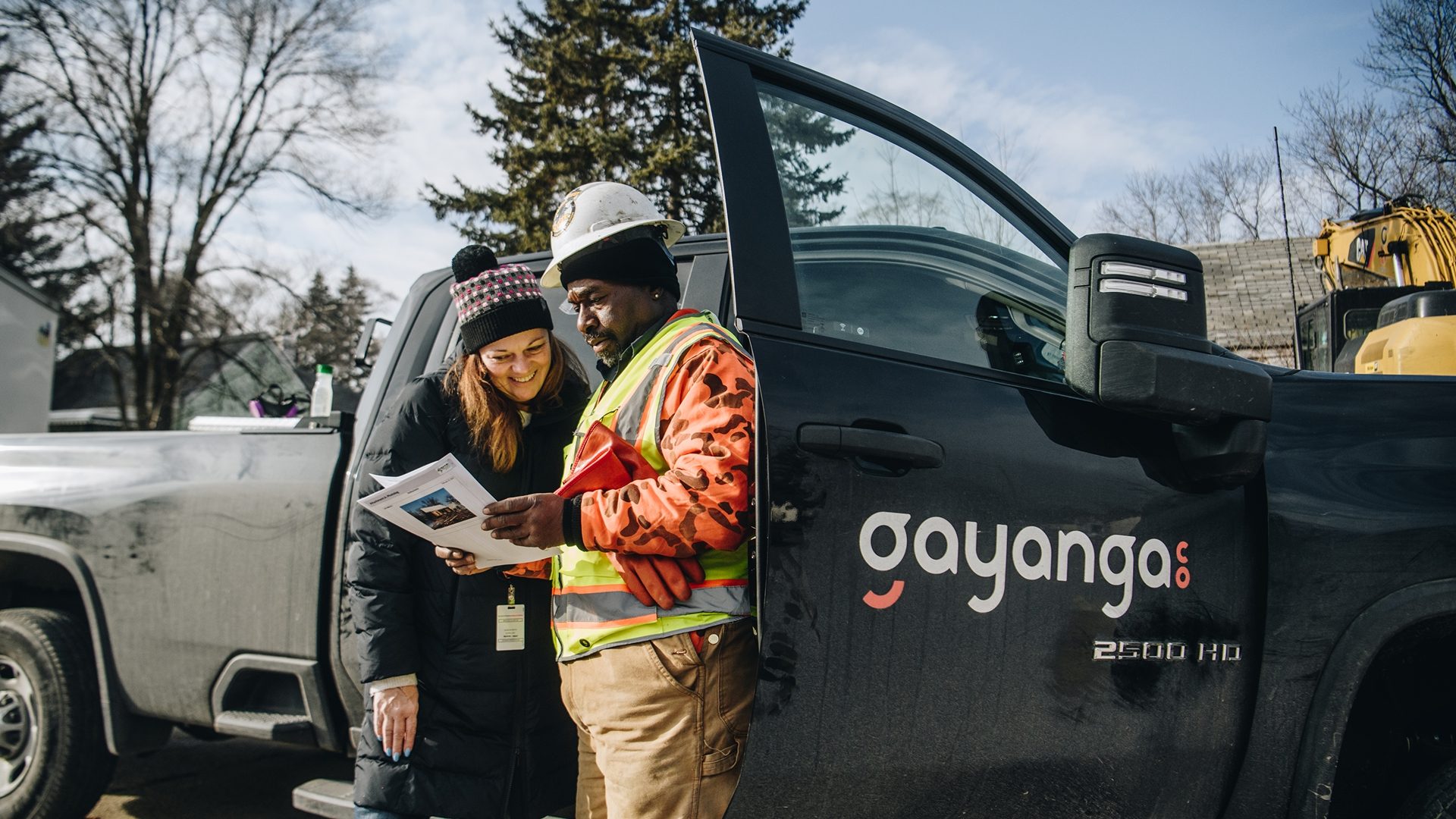 Gayanga Co. crew reviewing plans beside a company truck on a Detroit job site